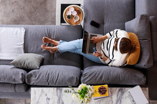 Young woman using her credit card and laptop to shop online while relaxing at home. Top view