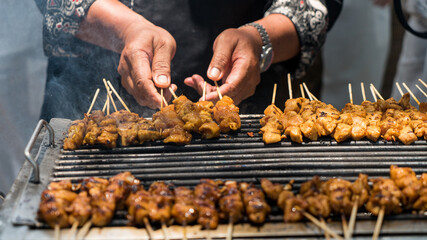 Chicken grilled satay skewers on fire with smoke. hands cooking satay on the grill. Asian style food.