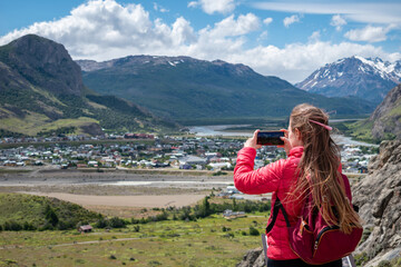 Mujer tomando una fotografía de El Chalten con su celular, desde el mirador nido del águila. Patagonia Argentina 