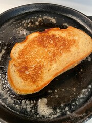 A perfectly grilled grilled cheese sandwich browning in sizzling butter on a cast iron skillet. 