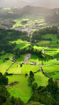 Aerial shot of green meadows, mountains and Furnas city on Sao Miguel Island, Azores, Portugal. Azores nature on sunny day. Vertical screen 