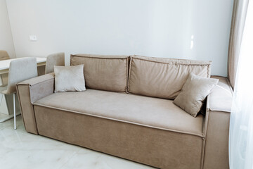 A brown couch made of composite material sits in a living room next to a window