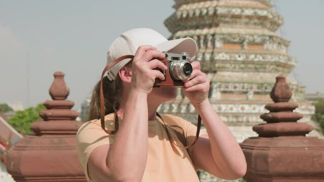 Tourist photographer taking pictures with analog retro camera of famous Wat Arun Buddhist temple of Dawn in Bangkok.