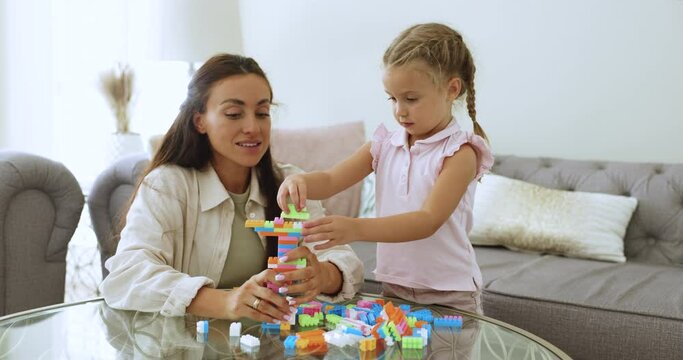 Mother spend quality time with preschooler 4s daughter, play together bricks, praises her for patience, giving high five, enjoy playtime and friendly relations. Motherhood, babysitting, family pastime