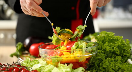 Cook holds fork in hand and mixes salad fresh vegetables seasoned with olive oil. Raw food and...