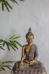 Estatua de Buda dorada en fondo blanco.
La estatua está ubicada contra un fondo blanco texturizado...