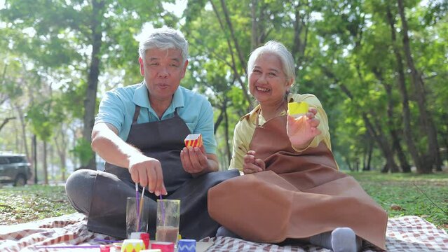 An elderly Asian couple does art activity painting ceramic pots in the garden outside. Living happily in retirement. art therapy