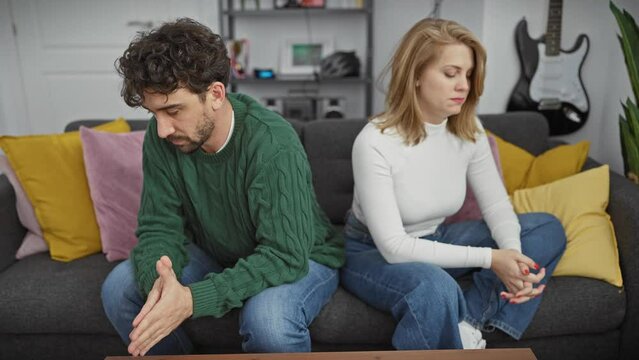 A man and a woman sitting apart on a couch in a living room, displaying tension and disconnection with a blurred background.