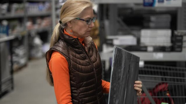 Mature woman inspects a sample of lvt, luxury vinyl tile in a hardware store for a home renovation project.
