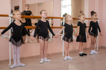Fototapeta premium Children's ballet school. Caucasian woman teaching ballet to little girls. 