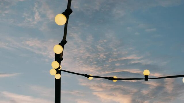 a garland of light bulbs burns near the pier at sunset
