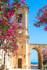 Picturesque photograph of a stone church with pink oleander flowers in the foreground and bright...