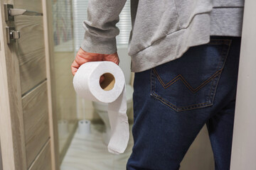 An older man's hand holding a roll of toilet paper in front of the toilet.