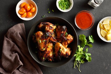 Grilled chicken wings in bowl over dark stone background. Top view, flat lay