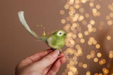 Cute decorative canary on a person&rsquo;s fingers, warm festive background.