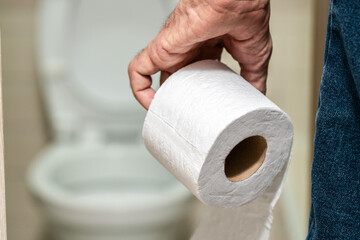 An older man's hand holding a roll of toilet paper in front of the toilet.