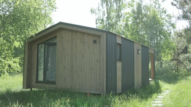 Modern Tiny House in grassy field is surrounded by trees and plants