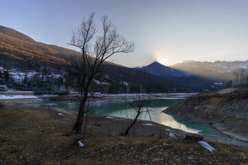 Winter sunset behind a mountain peak of a winter alpine landscape with reservoir lake at Barcis,...