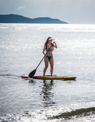 Young beautiful woman on stands up paddleboard surfer on a beautiful sunny day