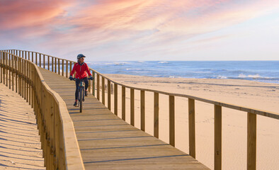 happy active senior woman cycling during moody golden hour at the beach of the atlantic coast of...
