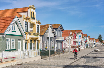 nice woman cycling with her electric mountain bike in front of the colorful wooden houses of Costa Nova do Prado near Aveiro, Portugal