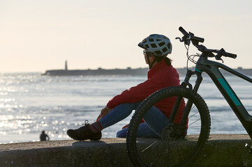 happy active senior woman cycling during moody golden hour at the beach of the atlantic coast below...