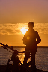 happy active senior woman cycling during moody golden hour at the beach of the atlantic coast below...