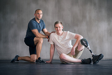 Trainer, person with a disability and prosthetic leg and posing in physiotherapy, studio and gym ball. Male people, physiotherapist and amputee for wellness, fitness and exercise in sports center