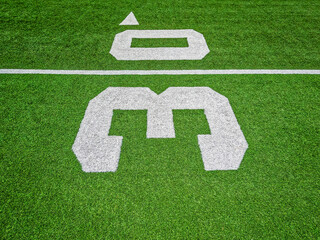 Football Field Turf. Bright green turf football field surface with white yard line markings. Focus on the thirty yard line marker. Overhead view. - Powered by Adobe