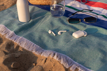 Wireless headphones, glass of water and sunglasses on the striped towel on the sand. Summer vacation lifestyle concept