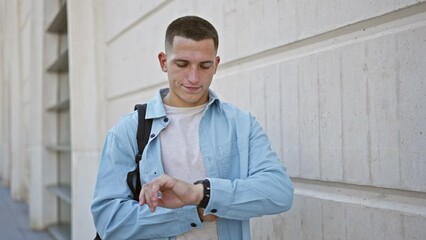 A young hispanic man checks the time on his watch against a university backdrop, conveying a sense of urgency and punctuality.