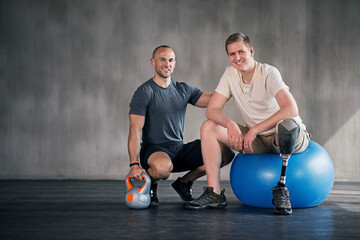 Physiotherapy, kettlebell and man with disability for fitness, training and muscle strength with coach for support. Amputee, exercise ball and physiotherapist for physical rehabilitation with workout - obrazy, fototapety, plakaty
