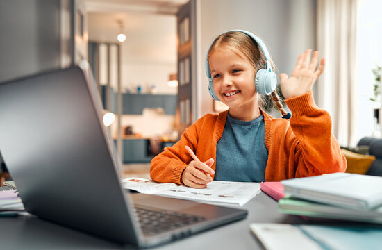 Concept of online classes. Positive kid in headset raising hand with greeting gesture at beginning of remote lesson