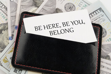 BE HERE, BE YOU, BELONG Words written on a business card in a leather accessory on the background...
