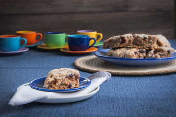 Serving of fruit biscuit cake on a table with colourful cups and saucers