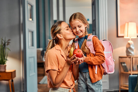 Healthy snack for pupil. Adult woman giving daughter apple and banana for healthy meal