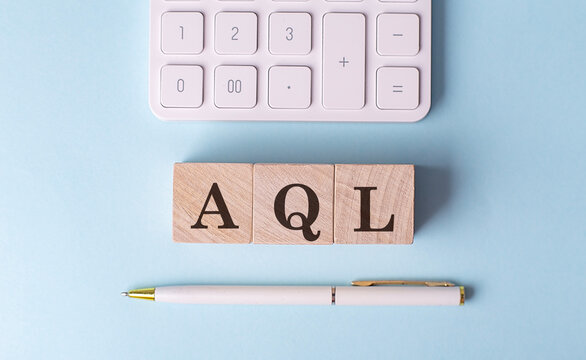 AQL word on wooden block with pen and calculator on blue background
