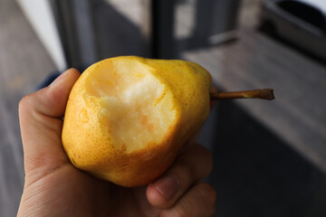 Photograph of a pear bitten and held in an unknown hand. Concept of healthy food and fruits.