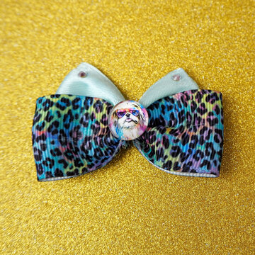 A blue leopard bow decorated with shiny stones and an insert with the image of a Shih tzu dog in the middle are depicted on a golden background. view from above. accessories for long-haired pets. top 