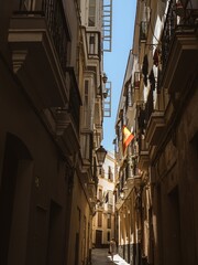 A young woman tourist in a blue dress walking down a narrow old town street in Cadiz under a Spanish flag, Andalusia, Spain
