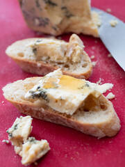 Stilton Blue Cheese with a drizzle of Honey on a French Baguette. Red Cutting Board.