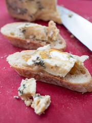 Stilton Blue Cheese with a drizzle of Honey on a French Baguette. Red Cutting Board.