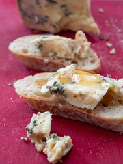 Stilton Blue Cheese with a drizzle of Honey on a French Baguette. Red Cutting Board.