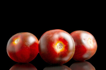 Three black cocktail tomatoes, macro, isolated on black background.