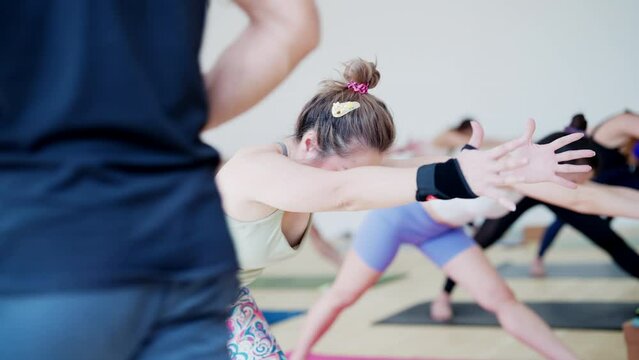 A woman is doing yoga poses with other people in a room. Scene is calm and focused, as everyone is concentrating on their poses