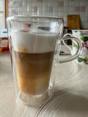 Coffee with milk poured from a coffee machine into a transparent, double-walled thermal mug