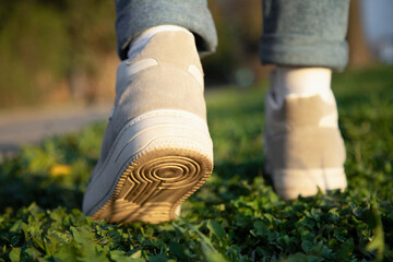 Rear view of female legs in jeans and sneakers walking on grass