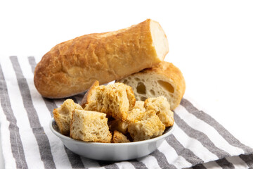 owl of seasoned croutons with the French bread used to make the croutons on a striped cloth isolated on white