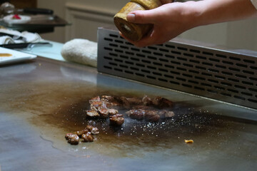 close up of seasoning and adding black pepper for small pieces of wagyu beef grilling on a stove in...