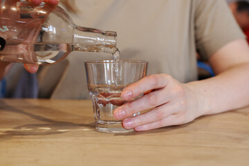 Hand pouring water from bottle into glass at wooden table